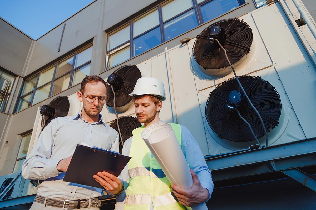 Service engineers in uniform inspecting industrial refrigeration system, outdoor refrigeration plant