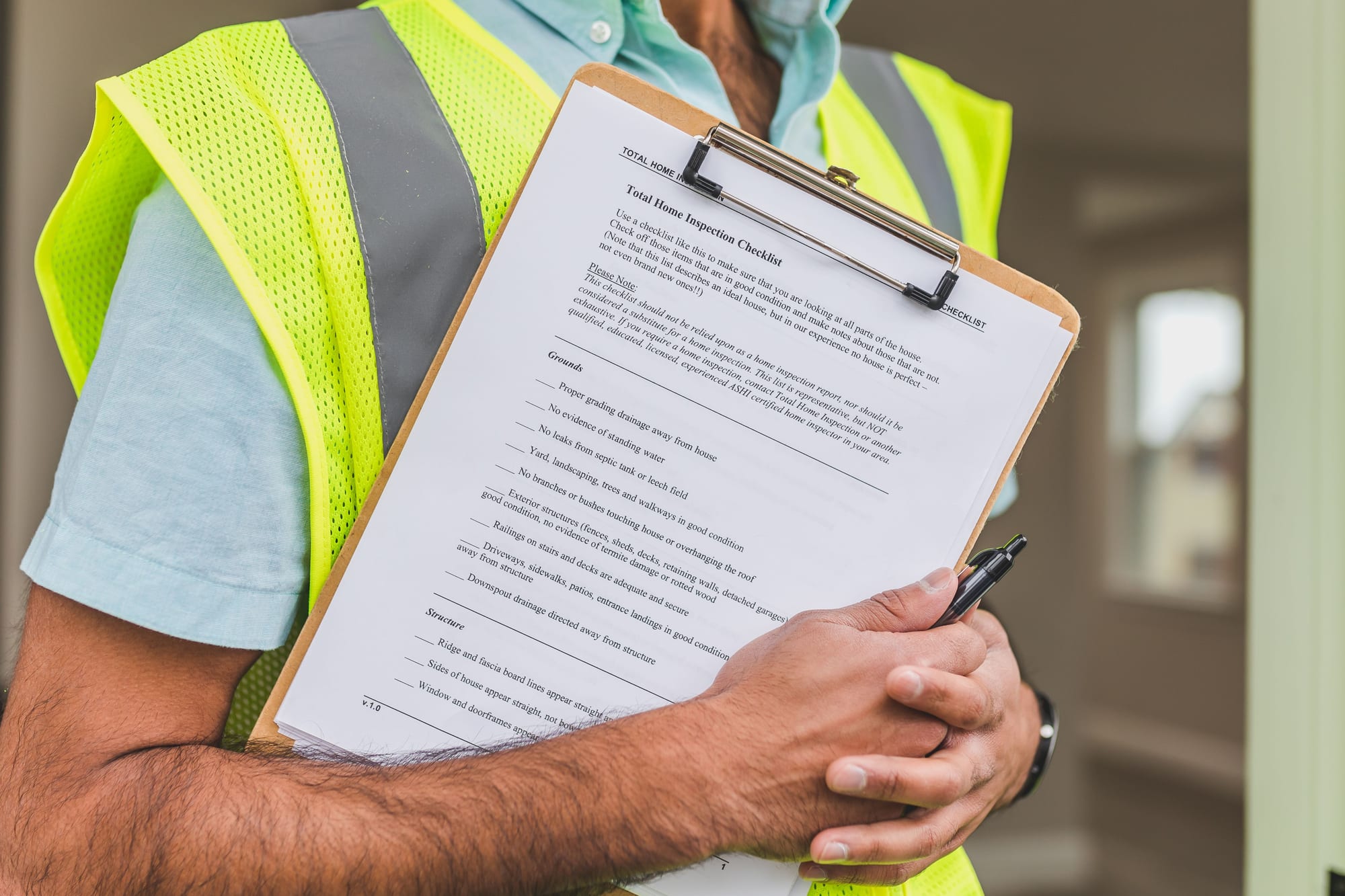 A building inspector reviewing a clipboard checklist while writing notes for an inspection report