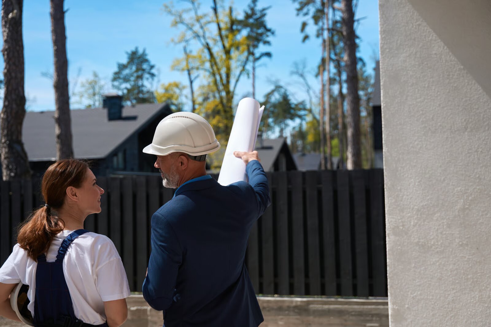 A building inspector in a hard hat holding plans while discussing a property with a client
